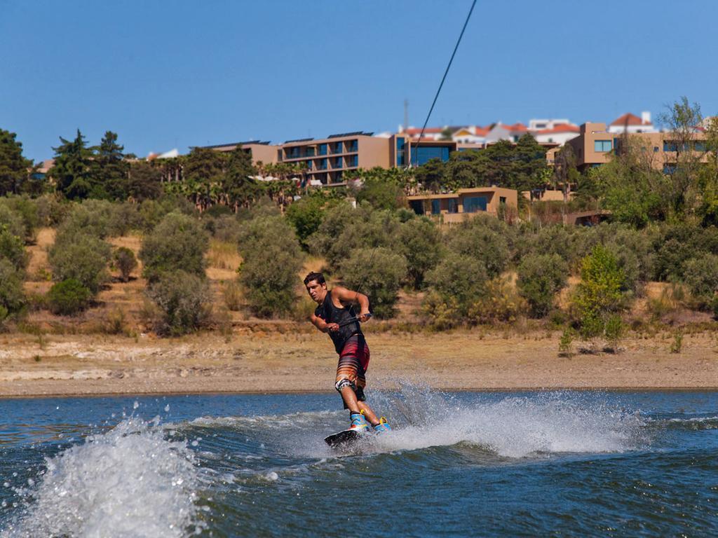 Ap Lago Montargil - Conference & Spa Экстерьер фото The photo shows a person wakeboarding on a body of water. The individual is being pulled by a cable, which is likely connected to a boat or a winch. The person is wearing a life jacket and swim shorts, balancing on the board as they enjoy the activit