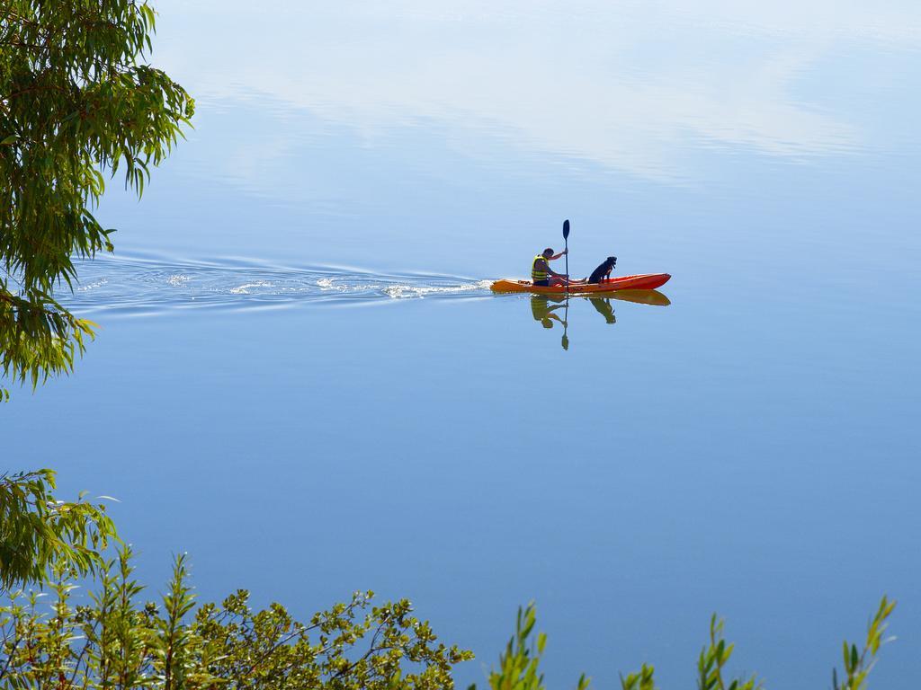 Ap Lago Montargil - Conference & Spa Экстерьер фото The photo shows a serene scene of a person kayaking on a calm body of water. The surface of the water is very smooth, reflecting the surroundings, and there is a gentle wake behind the kayak indicating movement. The kayaker is wearing a life jacket a