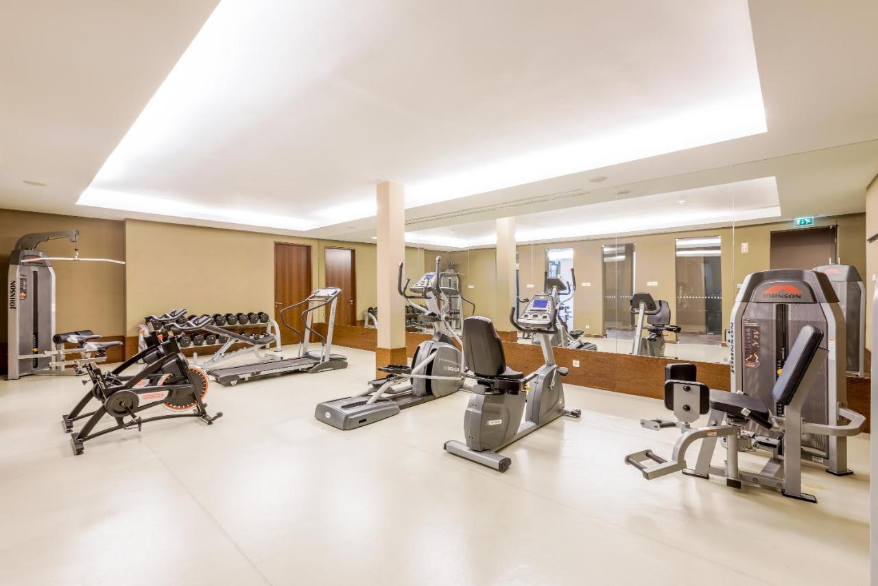 Ap Lago Montargil - Conference & Spa Экстерьер фото The image shows a modern gym interior featuring various exercise equipment. On the left, there are free weights and weight benches. In the center, there are multiple machines, including a stationary bike and an elliptical. The space is well-lit with 