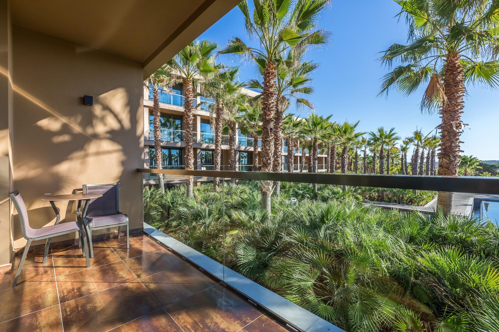 Ap Lago Montargil - Conference & Spa Экстерьер фото The photo shows a balcony with modern furniture, including a chair and a small table. In the background, there are tall palm trees and lush greenery, suggesting a tropical or resort-like setting. The buildings in the distance are likely part of a hot