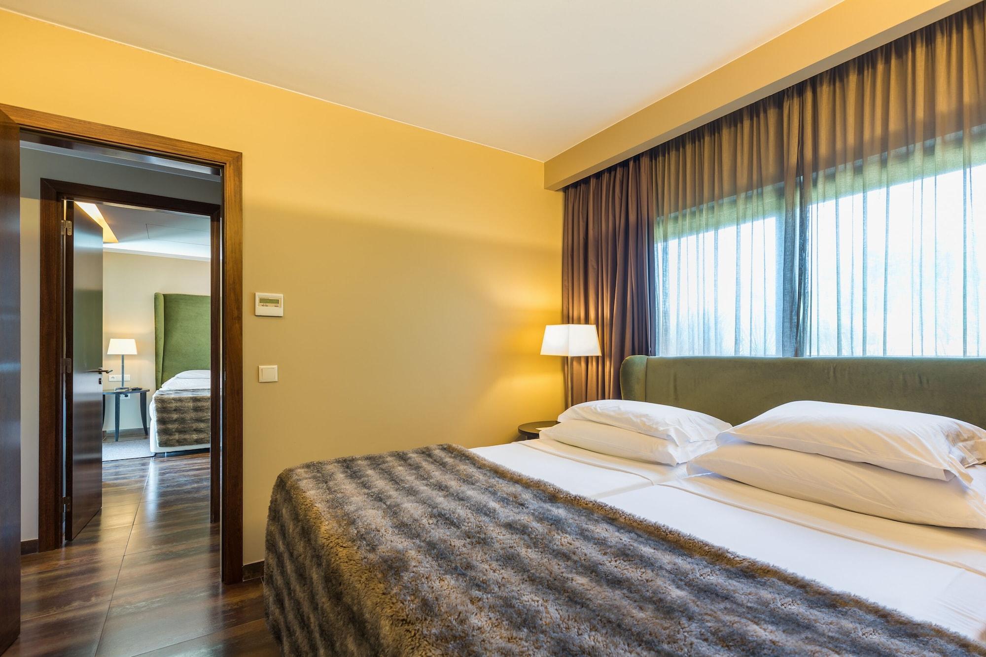 Ap Lago Montargil - Conference & Spa Экстерьер фото The photo shows the interior of a well-furnished hotel room. It features two beds with white linens and a gray decorative throw on top. The walls are painted a warm yellow, and there are floor-to-ceiling windows covered with dark curtains that allow 