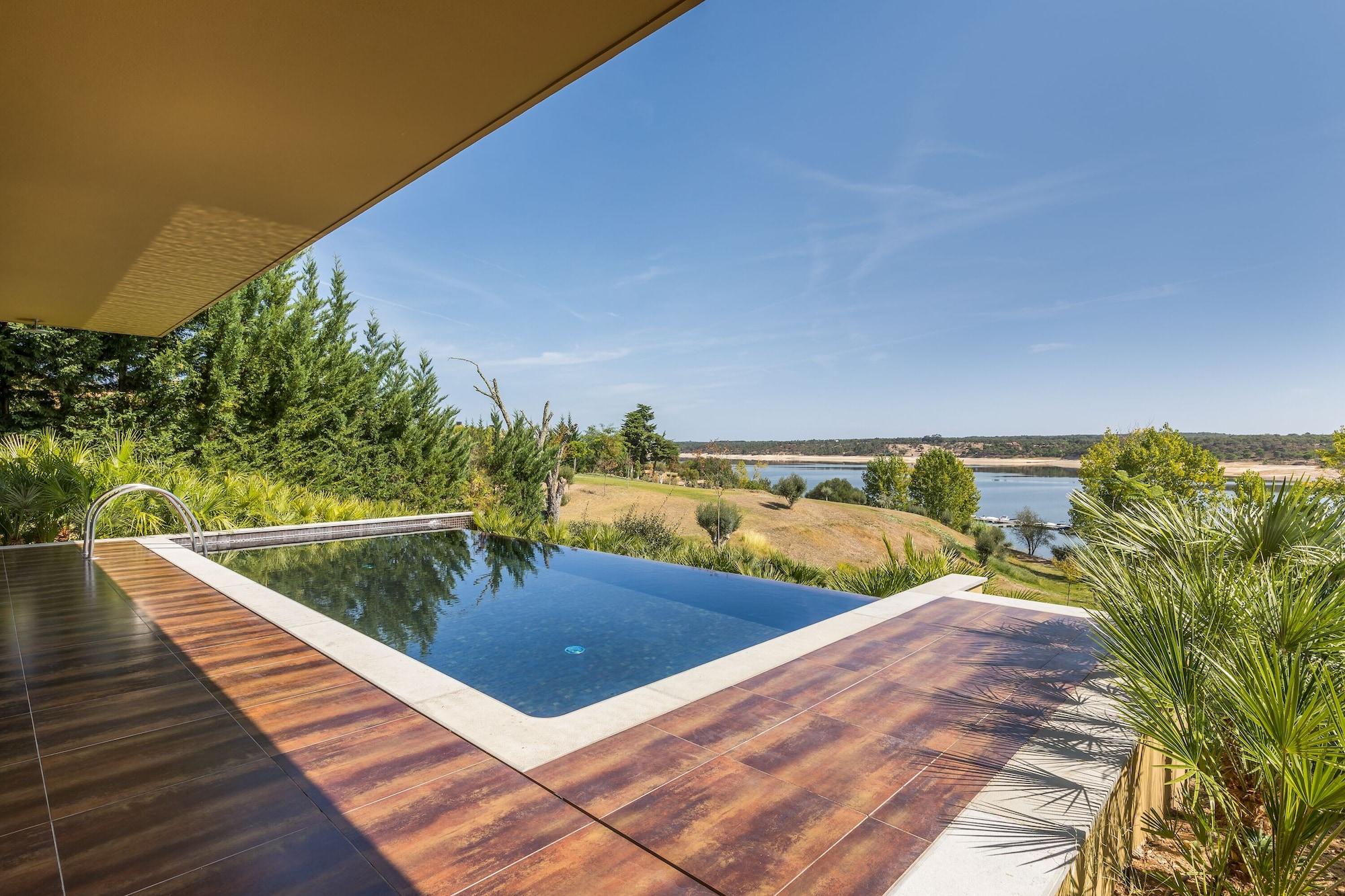 Ap Lago Montargil - Conference & Spa Экстерьер фото The photo shows a luxurious infinity pool situated on a terrace or deck. The pool features a sleek, modern design with a dark blue surface that reflects the surrounding scenery. In the background, there is a landscape of rolling hills and a body of w