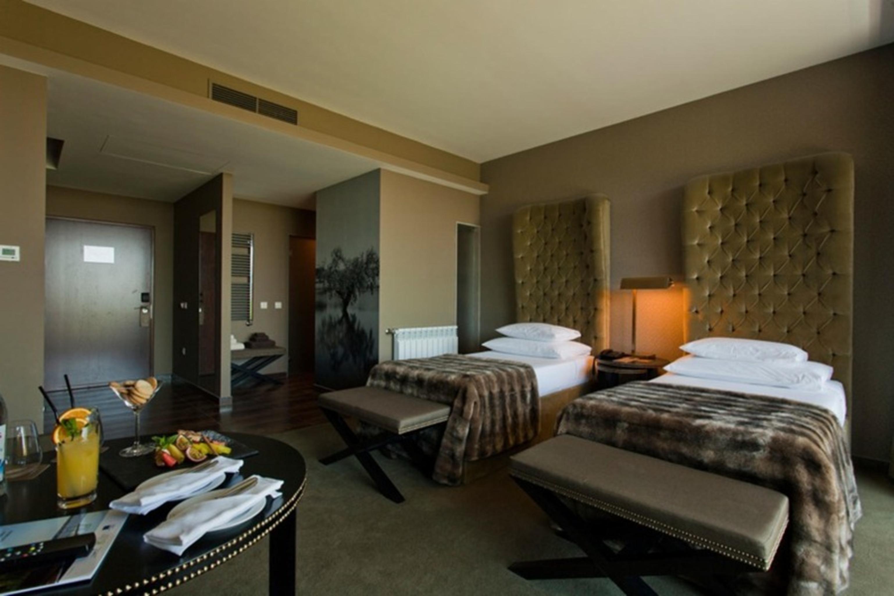 Ap Lago Montargil - Conference & Spa Экстерьер фото The photo shows a stylish hotel room featuring two beds with plush, upholstered headboards. The room has a modern and elegant design, with earthy tones dominating the decor. A small round table is set up in the foreground, displaying a drink and some