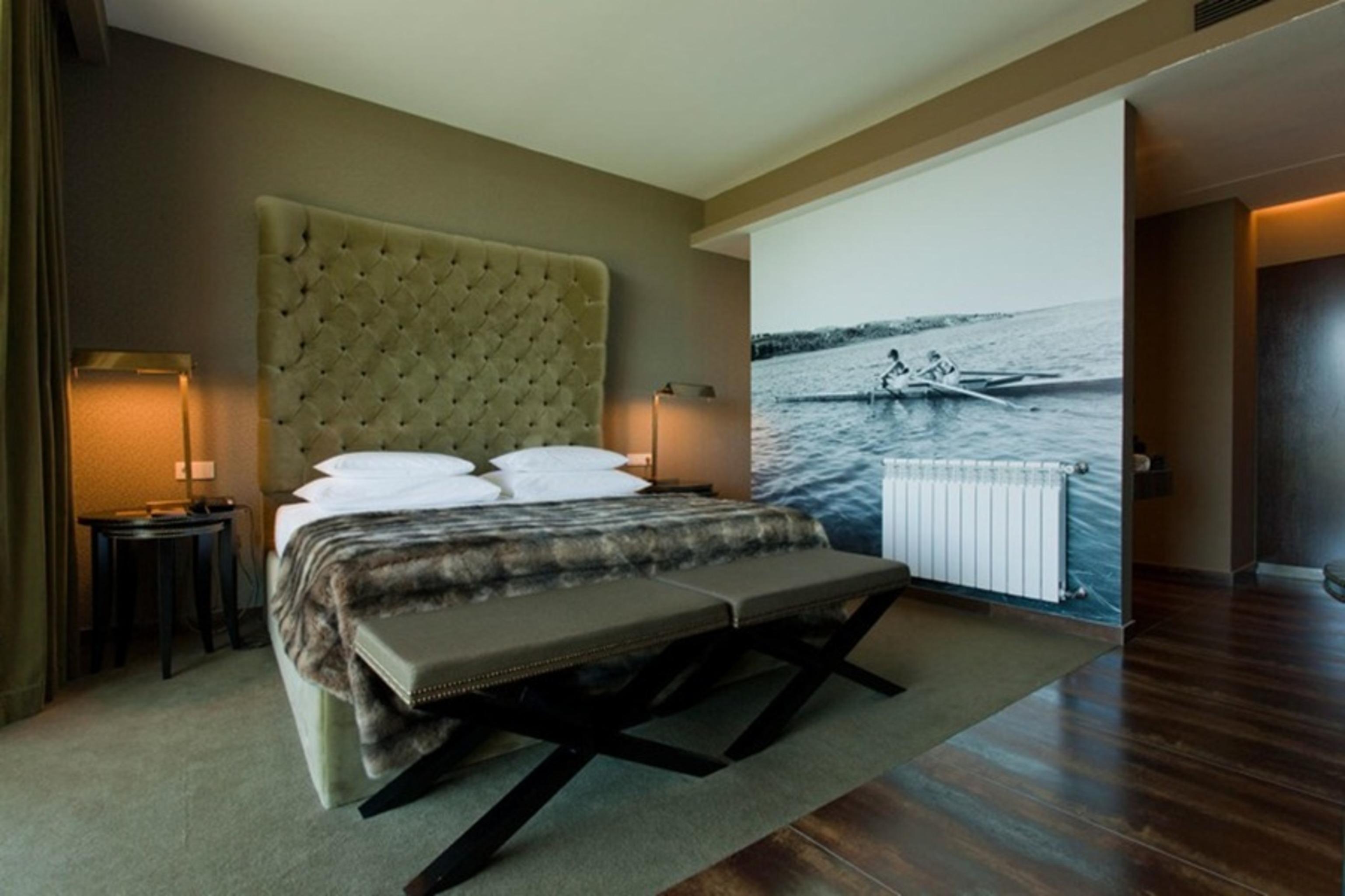 Ap Lago Montargil - Conference & Spa Экстерьер фото The photo shows a modern hotel room featuring a large bed with a tufted headboard and plush bedding. The color palette is neutral, with shades of green and gray. On one side of the room, there are bedside tables with lamps. A comfortable bench sits a