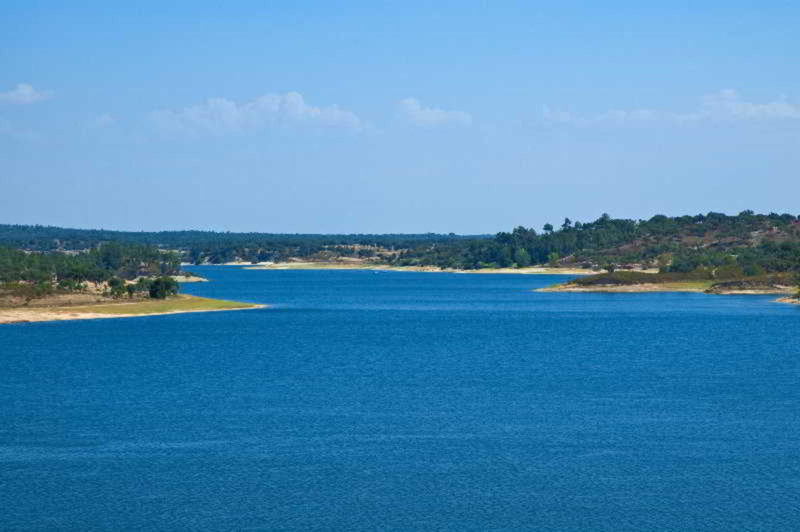 Ap Lago Montargil - Conference & Spa Экстерьер фото The photo depicts a serene landscape featuring a large body of water, likely a lake or river. The water appears calm and is reflecting a clear blue sky with some clouds. Surrounding the water, there are patches of green land and trees, indicating a n