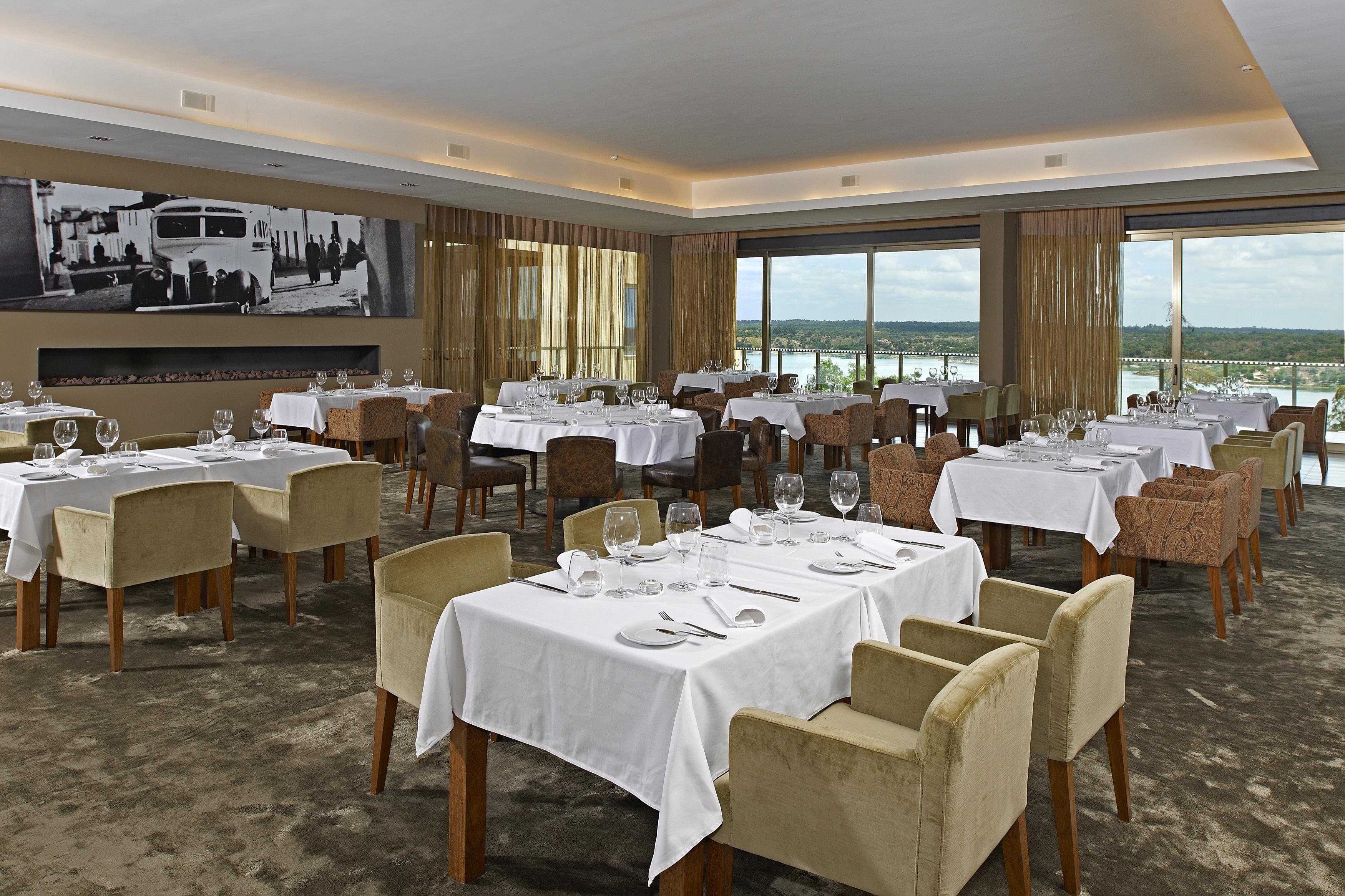 Ap Lago Montargil - Conference & Spa Экстерьер фото The photo shows an elegant restaurant interior featuring neatly arranged tables with white tablecloths. Each table is set with plates, cutlery, and glasses. The seating includes a mix of upholstered chairs in different colors—some light and others da