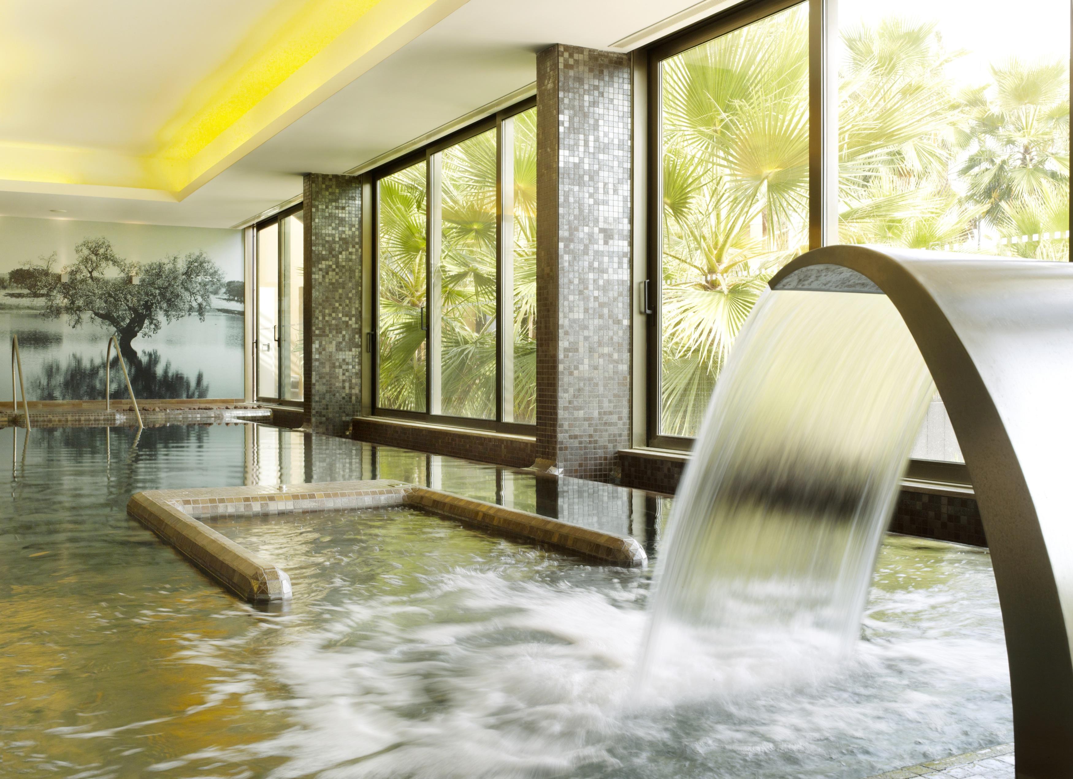 Ap Lago Montargil - Conference & Spa Экстерьер фото The photo depicts a serene spa environment featuring a tranquil indoor pool area. There is a sleek, modern water feature that spills water gracefully into the pool. Large windows allow natural light to flood the space, showcasing views of lush greene